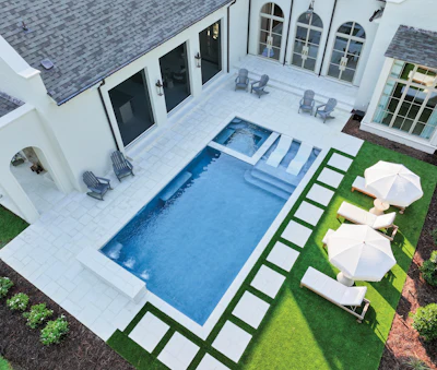 Aerial view of modern white house with rectangular pool, patio seating, and manicured lawn with umbrellas