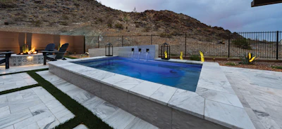 Modern luxury pool with white patio, lounge chairs, and hillside landscape at dusk