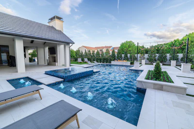 Modern luxury home with resort-style swimming pool, spa, lounge chairs, and manicured landscaping