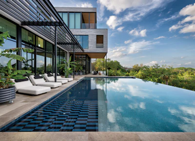 Modern luxury home with infinity pool overlooking landscape and blue sky