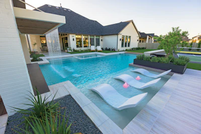 Modern luxury home with resort-style swimming pool and spa featuring lounge chairs and landscaping