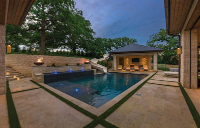 Luxury backyard with illuminated swimming pool, modern pool house, and outdoor patio at dusk