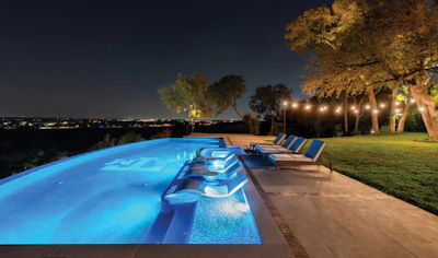 Illuminated luxury swimming pool with lounge chairs overlooking city lights at night