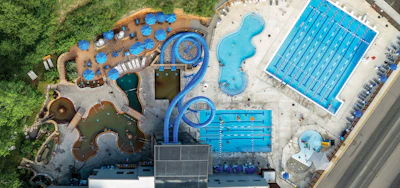 Aerial view of aquatic recreation center with Olympic-size pools, water slides, and children's play area surrounded by green landscaping