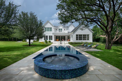 Modern white farmhouse with rectangular pool and circular fire pit on manicured lawn