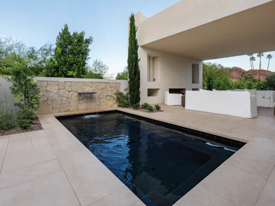 Modern minimalist home with rectangular black pool, stone accent wall, and desert landscape views
