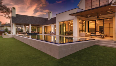 Modern luxury home exterior at dusk with illuminated windows, infinity pool, and manicured lawn