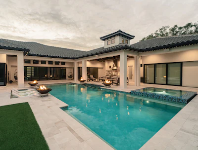 Modern luxury home with resort-style pool, spa, and covered patio overlooking manicured lawn at dusk