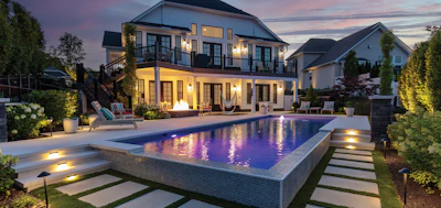 Luxury home with illuminated pool at twilight, featuring modern architecture and landscaped grounds