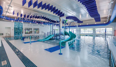 Modern indoor aquatic facility with turquoise water slides, diving platforms, and blue acoustic ceiling panels