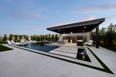 Modern luxury backyard with infinity pool, black pergola, lounge seating, and manicured landscape at dusk