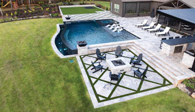 Aerial view of luxury backyard with blue swimming pool, fire pit seating area, and stone patio surrounded by manicured lawn.