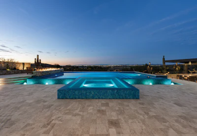 Luxury rooftop pool with turquoise water and geometric design illuminated at twilight, overlooking desert landscape.