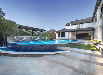 Luxury backyard with curved blue swimming pool, modern house, concrete patio, and pergola structure