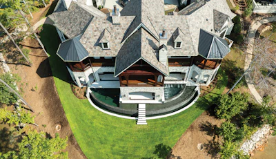 Aerial view of a modern curved residential estate with multi-level roofing, manicured lawn, and surrounding trees