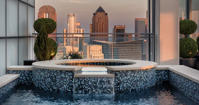 Modern rooftop spa with blue mosaic hot tub overlooking downtown city skyline at sunset