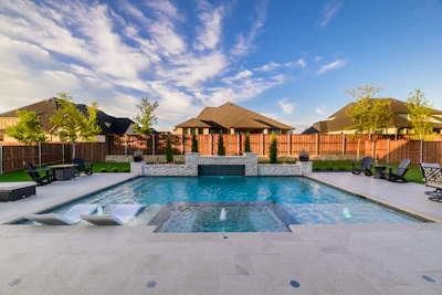 Luxurious backyard swimming pool with spa features, stone fireplace, wooden fence, and manicured lawn surrounded by residential homes