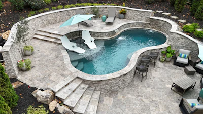 Aerial view of luxury backyard with curved swimming pool, stone patio, lounge chairs, and landscaping