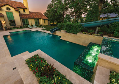 Luxury home with turquoise swimming pool, yellow Mediterranean-style architecture, and manicured landscaping at dusk