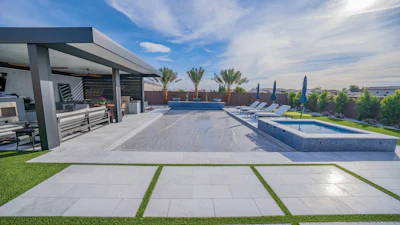 Modern luxury home with infinity pool, patio seating, manicured lawn, and mountain views under blue sky
