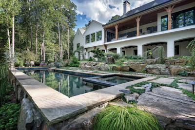 Modern white house with covered porch overlooking a rectangular reflecting pool surrounded by natural stone and landscaping