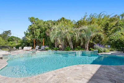 Luxury resort pool with crystal-clear turquoise water surrounded by palm trees and lounge seating under clear blue sky