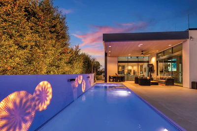 Modern home with illuminated pool at twilight, featuring decorative wall art and floor-to-ceiling windows