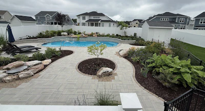 Backyard oasis with blue swimming pool, stone patio, fire pit, and landscaped gardens surrounded by residential homes