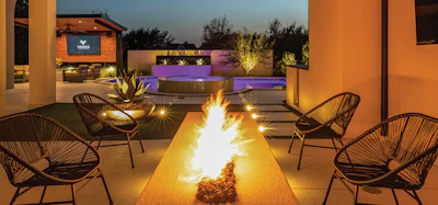 Modern outdoor patio with linear fire pit, black lounge chairs, warm lighting, and purple-lit architectural features at dusk