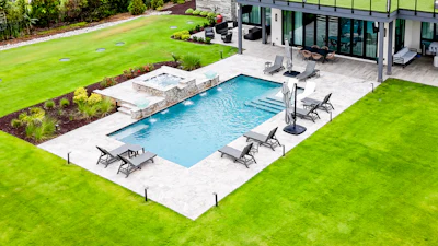 Modern backyard with rectangular swimming pool, lounge chairs, and manicured lawn adjacent to contemporary house