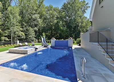 Luxury backyard with resort-style swimming pool, water slide, hot tub, and manicured lawn surrounded by trees