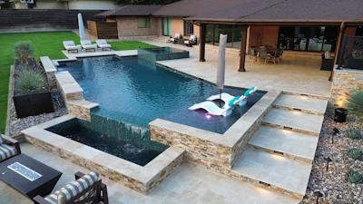 Luxury backyard with infinity pool, spa, lounge chairs, and modern patio overlooking manicured lawn