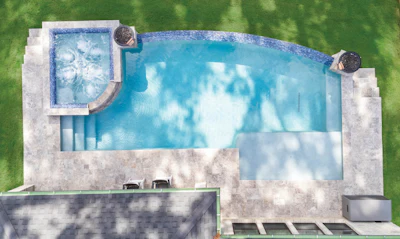 Aerial view of a residential pool with spa, concrete patio, and surrounding green lawn