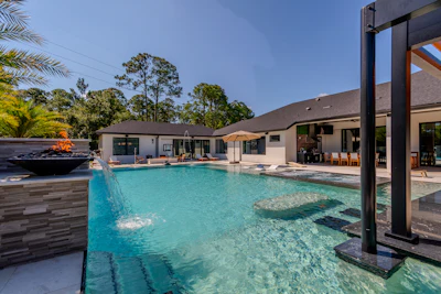 Modern luxury home with turquoise pool, fire pit, and open-concept patio overlooking landscaped grounds