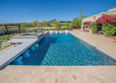 Luxury backyard with Olympic-length swimming pool, blue water, stone patio, lounge chairs, and vibrant pink flowering vines against desert landscape.