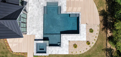 Aerial view of modern home with turquoise pool, wooden deck, white patio, and manicured landscaping