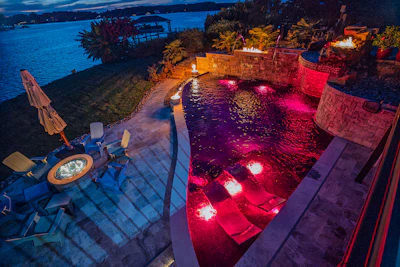 Luxury waterfront resort with illuminated pink-lit pools, stone terraces, and evening water views at dusk