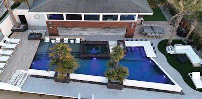 Aerial view of modern luxury home with illuminated blue swimming pool, palm trees, and manicured grounds