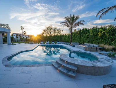 Luxury backyard with resort-style swimming pool, spa, lounge seating, and manicured landscaping at sunset
