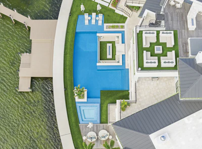 Aerial view of residential property with blue pools, manicured green lawns, white structures, and gray roofing