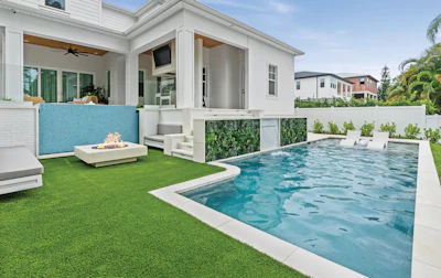 Modern luxury home with resort-style backyard featuring turquoise pool, artificial turf, fire pit, and contemporary white architecture