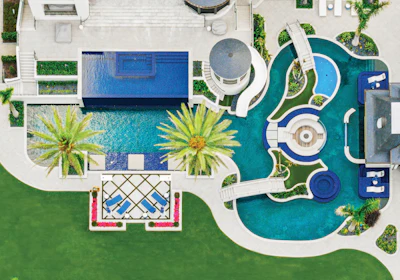 Aerial view of luxury resort with blue swimming pools, palm trees, white lounge chairs, and manicured green lawn