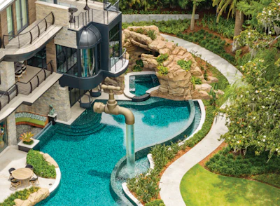 Aerial view of luxury home with turquoise infinity pool, stone waterfall feature, and manicured landscaping