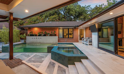 Modern brick home with covered patio, infinity pool, and sunken spa overlooking landscaped garden