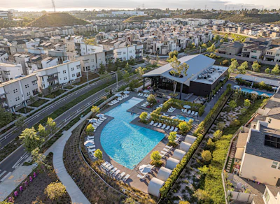 Aerial view of modern residential complex with blue swimming pool, lounge chairs, and surrounding apartment buildings in urban neighborhood