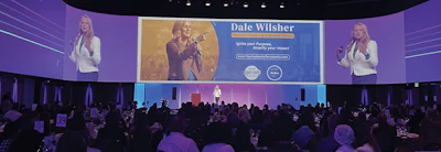 Conference stage with Dale Wilsher presentation banner and audience seated at tables under purple and blue lighting