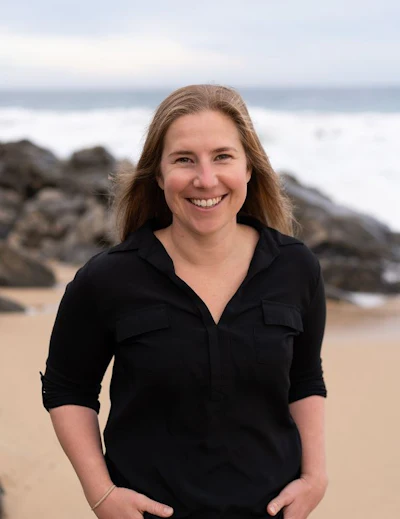 Woman smiling at beach with rocks and ocean waves in background
