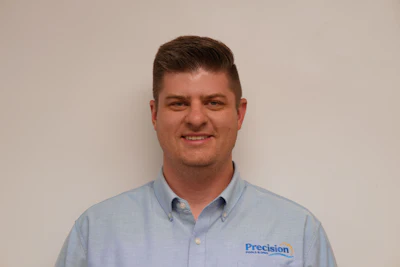 Professional headshot of man in light blue Precision branded shirt against neutral background