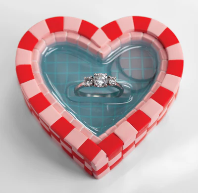 Diamond engagement ring displayed in red and pink checkered heart-shaped box with teal interior
