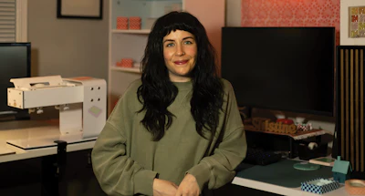 Woman with long black hair wearing olive green sweater sitting at desk in modern office workspace